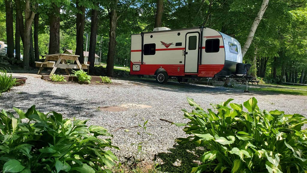 In a Spring campground trail, a red and white RV is parked among blooming flowers in a wooded area.