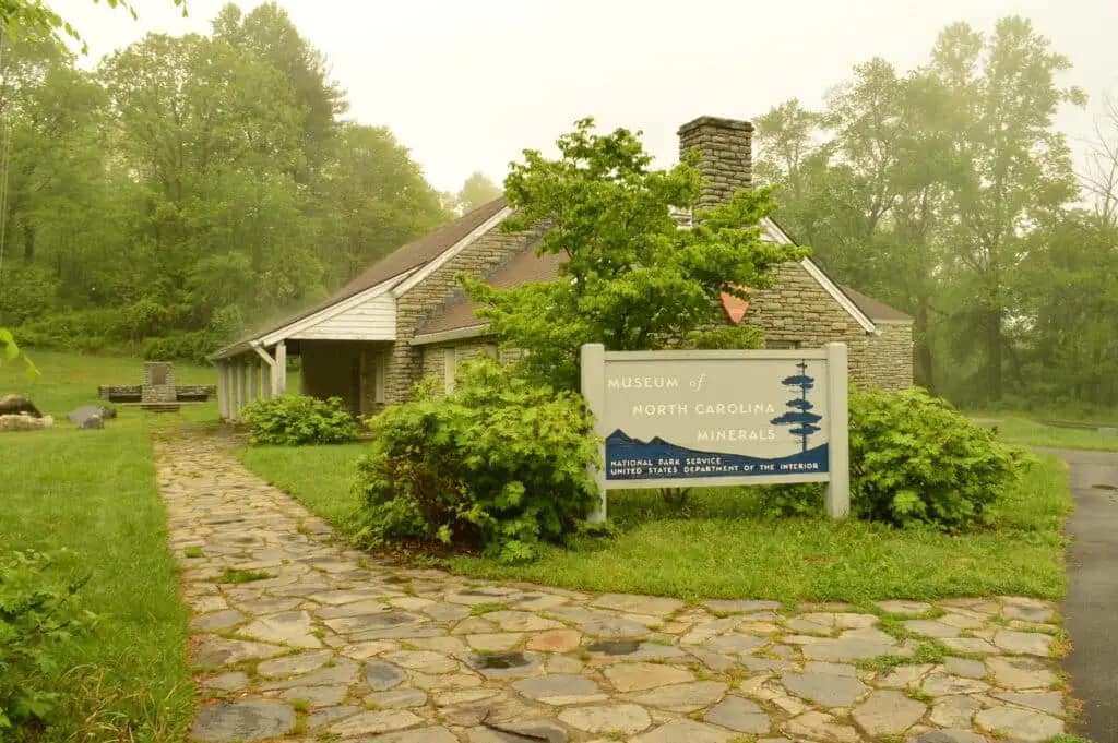 Stone building surrounded by greenery with a sign reading "Museum of North Carolina Minerals" in front, offering a picturesque setting that includes captivating waterfalls and vibrant wildflowers.