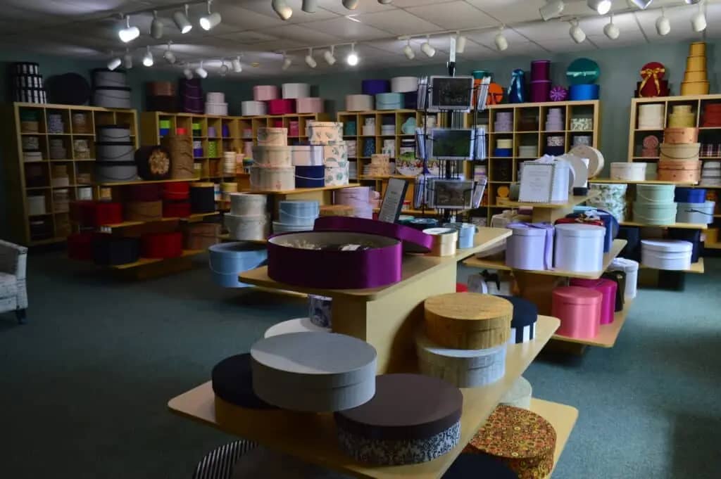A store interior filled with variously sized and colored round boxes arranged on shelves and tables. Bright lighting and an organized layout create a neatly displayed inventory reminiscent of the serene charm found at Seven Maples Campground in Hancock, NH.