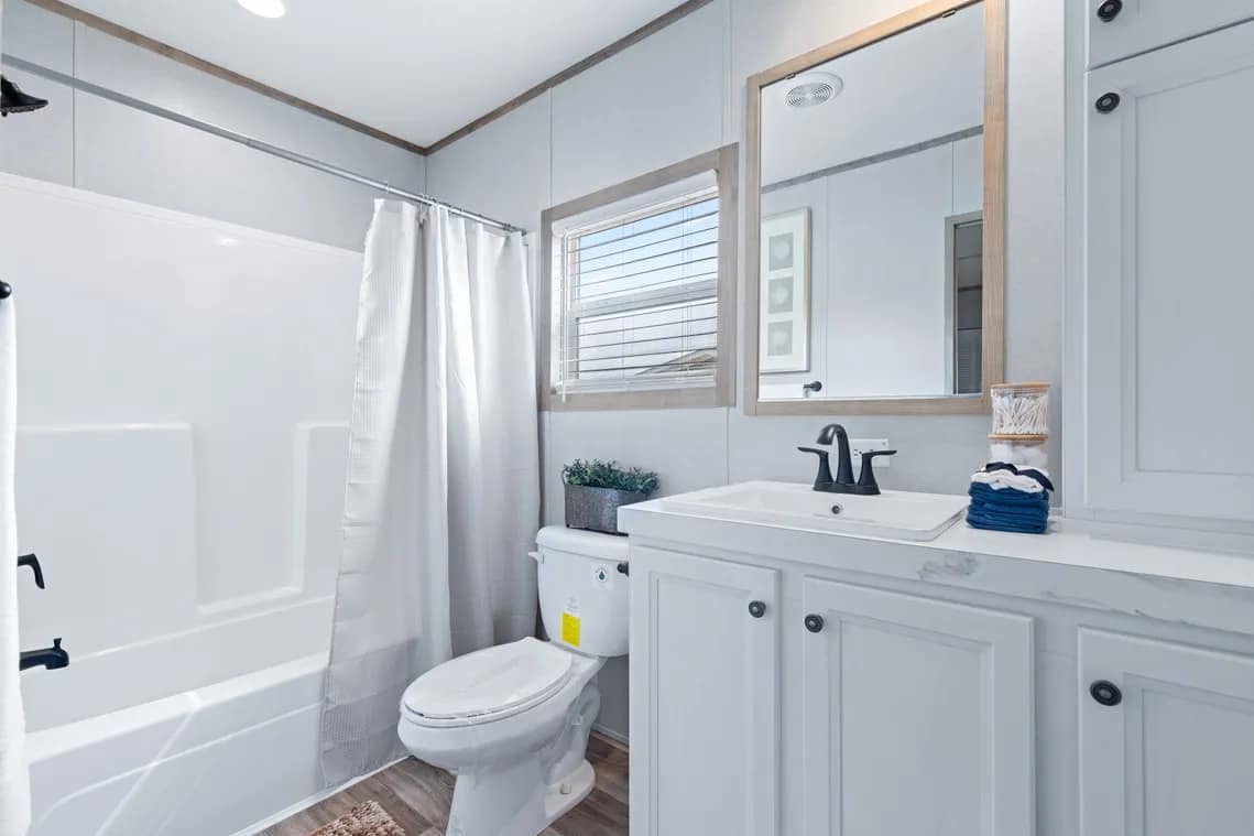 Modern bathroom with white cabinets, a sink with black fixtures, a toilet, a bathtub with a shower curtain, and a window above the toilet.