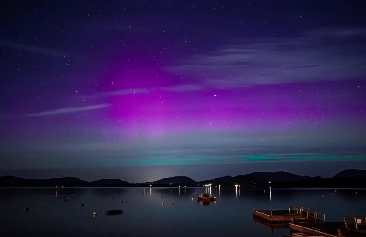 Stunning night view of aurora borealis with purple and green lights over a calm lake