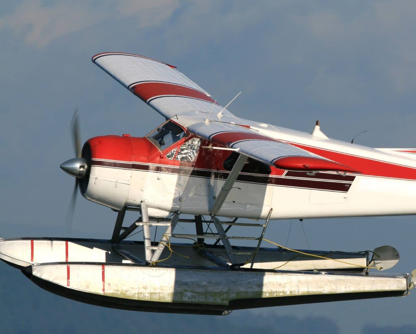 A red and white seaplane with a propeller glides effortlessly against the clear blue sky. This remarkable aircraft, equipped with pontoons for smooth water landings, promises an unforgettable fly-in experience.