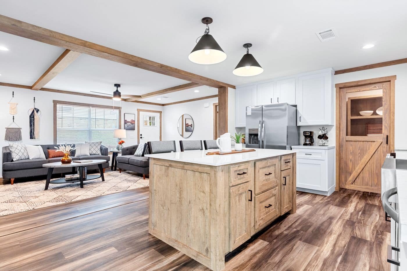 Open-concept kitchen and living room featuring a wooden island, stainless steel appliances, gray sectional sofa, and wood accents throughout.