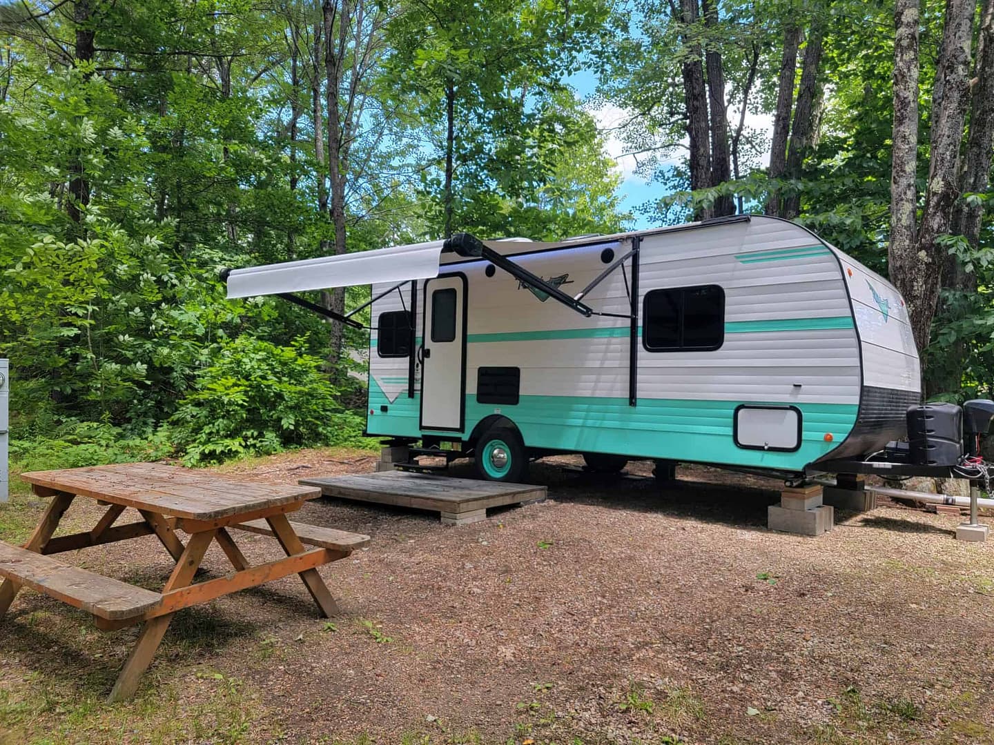 An RV parked in the woods near blooming flowers, perfect for a Spring getaway.