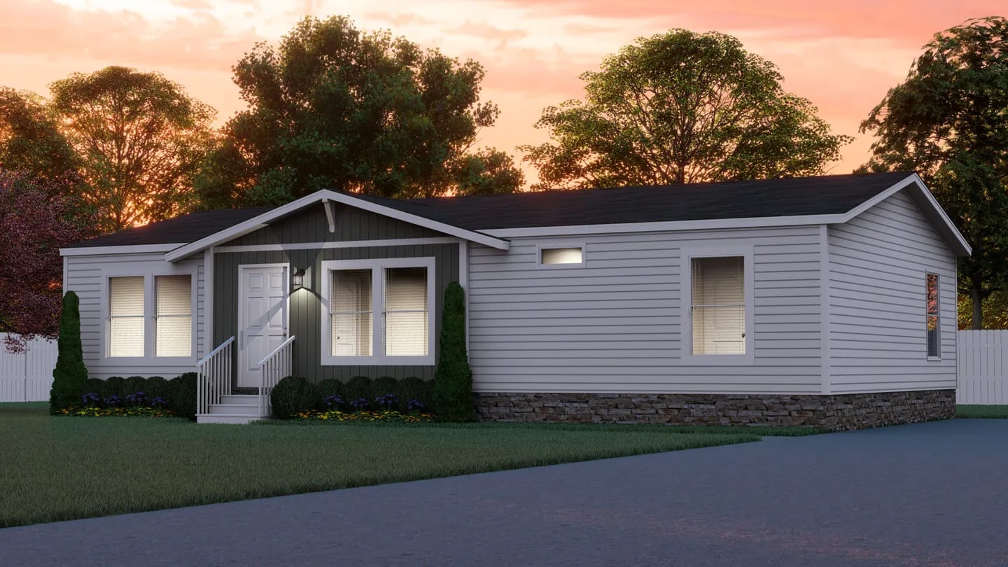 Single-story manufactured home with gray siding, stone trim, white-framed windows, small front porch, and landscaped yard, set against trees at sunset.