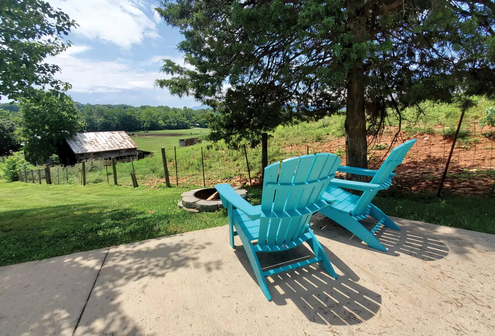 Blue adirondack chair on a patio overlooking scenic views of a farm with a wooden barn, green fields, and trees under spacious skies.