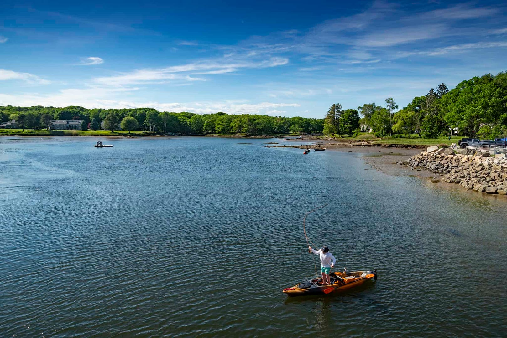 In the springtime, a man fishes from his kayak on the river.
