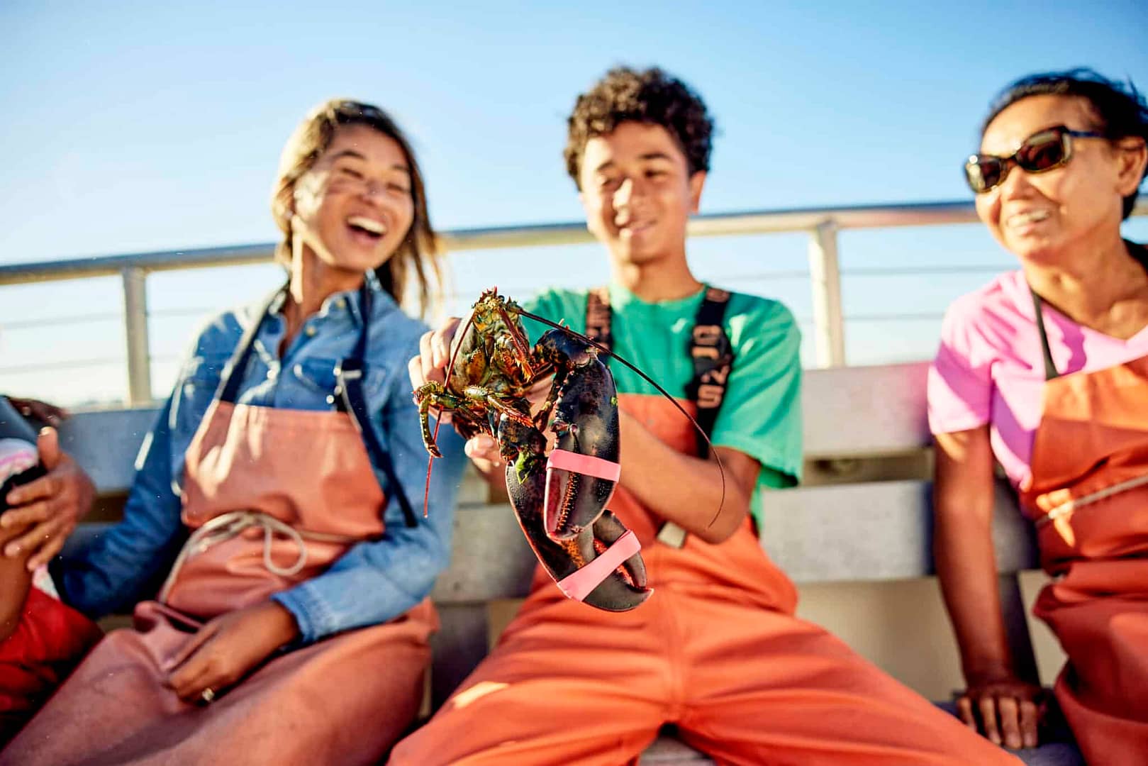 A group of people sitting on a bench holding lobsters at a campground.