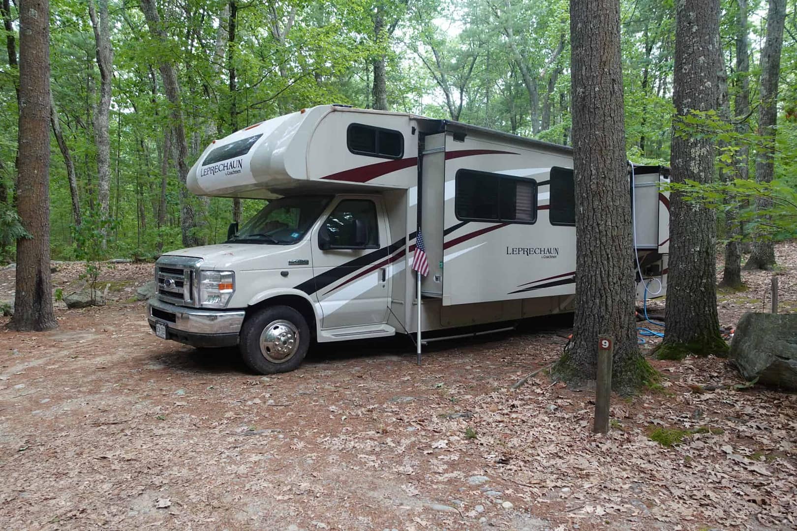 An rv parked in a wooded area near a campground trail, surrounded by blooming flowers.