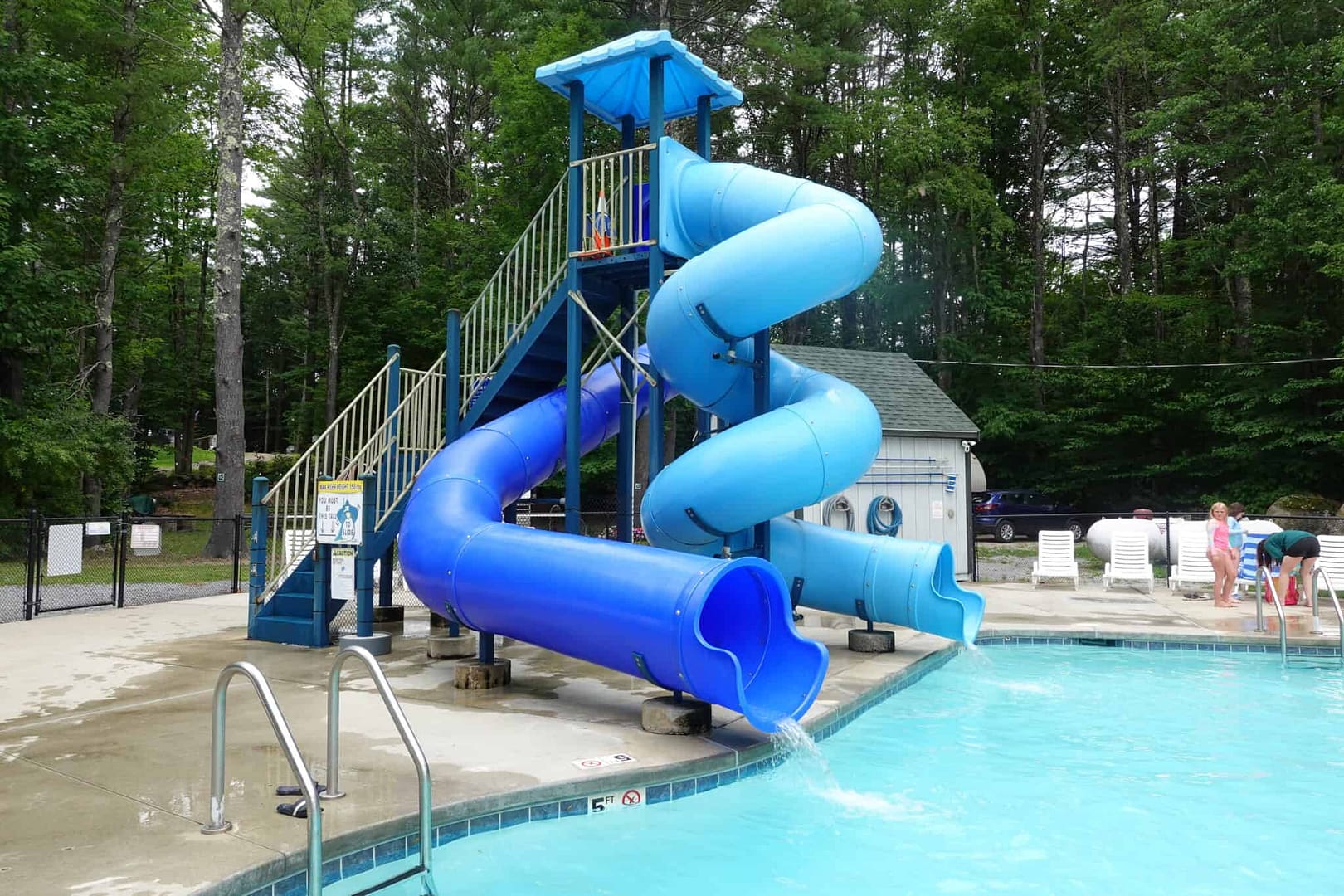 A blue water slide at a pool with blooming flowers nearby.