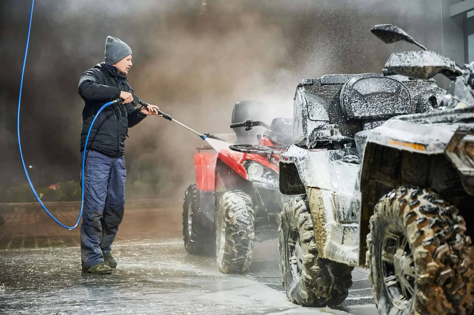 A man is washing his ATV with a hose near amenities.