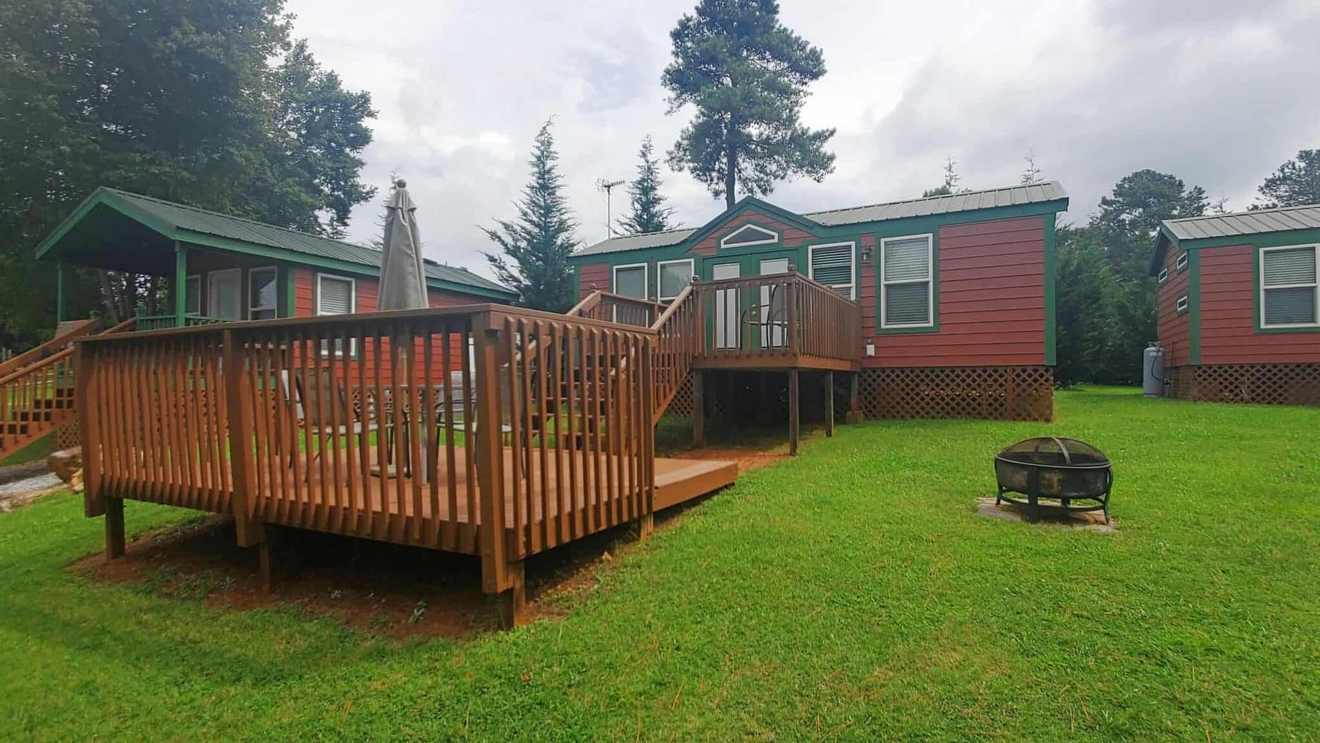 A small cabin in the woods with a deck, surrounded by blooming flowers.