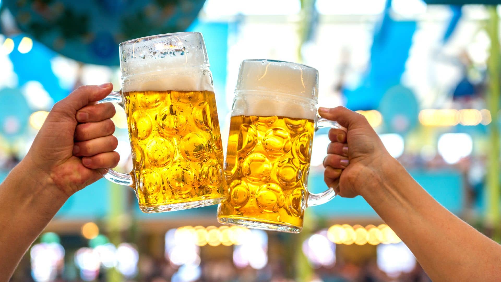 Two hands holding large, frothy beer steins clink together in a celebratory gesture at the Hub City Brew Fest. The background is a blurred, festive atmosphere suggesting an exciting festival setting.