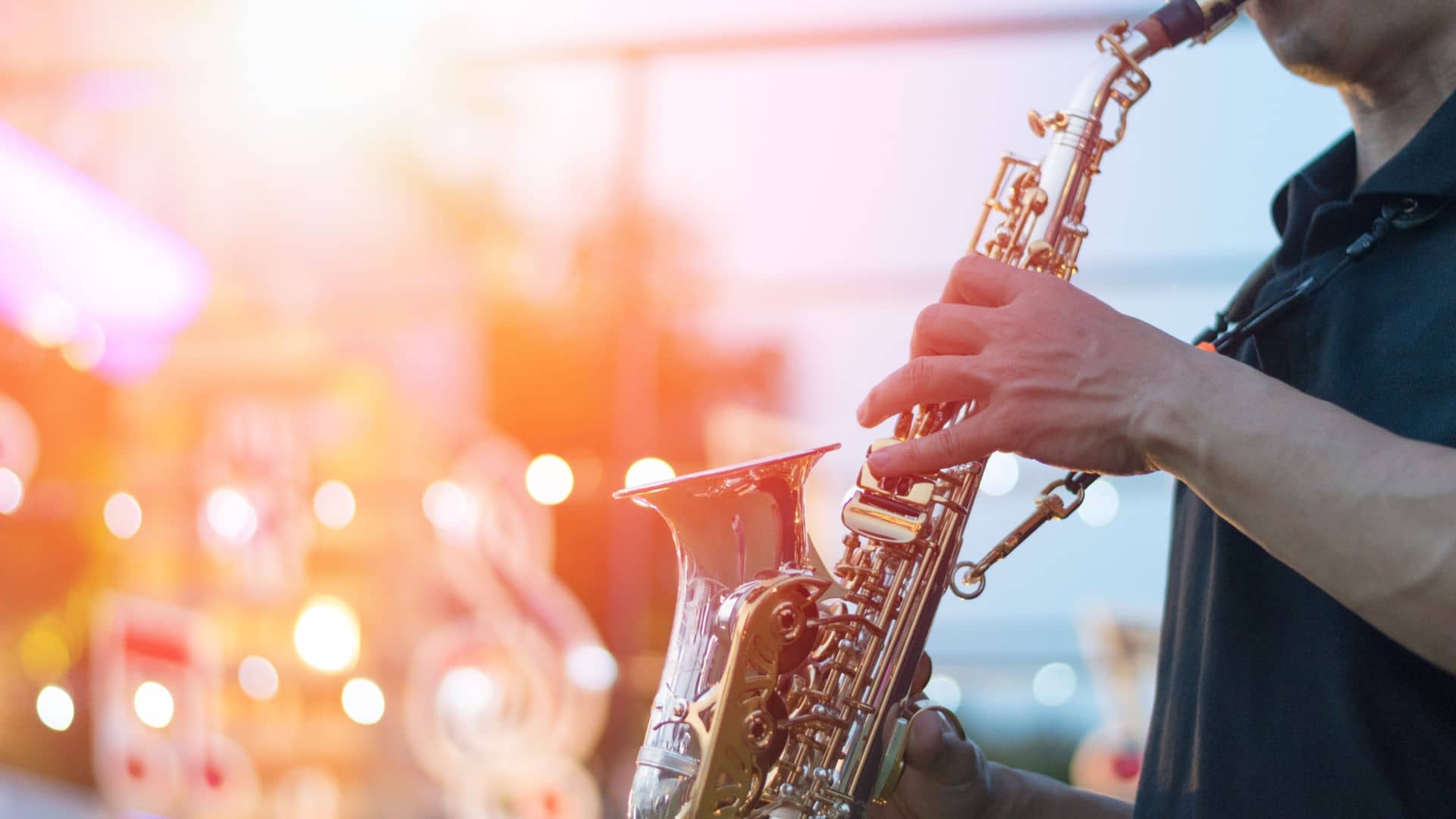 A person plays a saxophone outdoors in Greenville, surrounded by warm sunlight and soft-focus lights. The gleaming sax reflects the light, creating a lively jazz atmosphere that feels as if it's part of a vibrant festival you won't soon forget.
