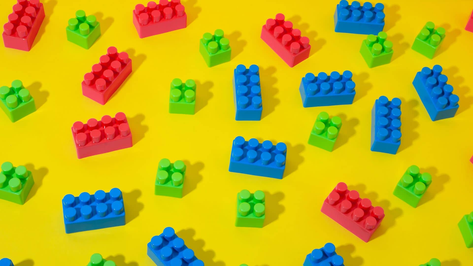 Assorted red, green, and blue toy building blocks scattered on a bright yellow background.