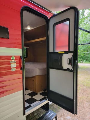A red and white rv with a black door open.