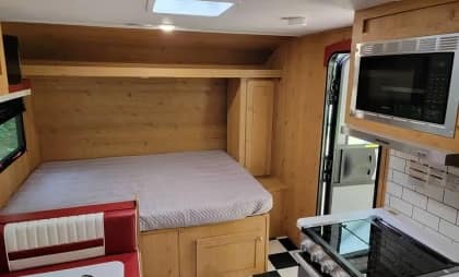 Compact motorhome interior with a bed, kitchenette, and seating area.