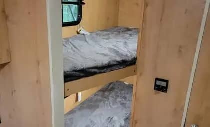 Interior of a compact living space with wooden bunk beds and a window on the top bunk.