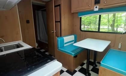 Interior of a vintage camper with a kitchenette, dining booth, and checkered floor.