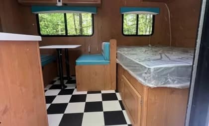 Interior of a vintage camper with checkerboard flooring, turquoise seating, and wooden cabinets.