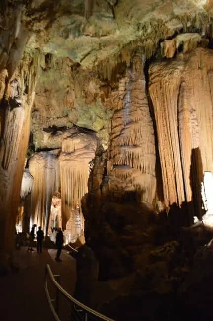 Visitors walk along a pathway inside a large cave with illuminated stalactites and stalagmites, reminiscent of the awe-inspiring wonder found in the Shenandoah Views.