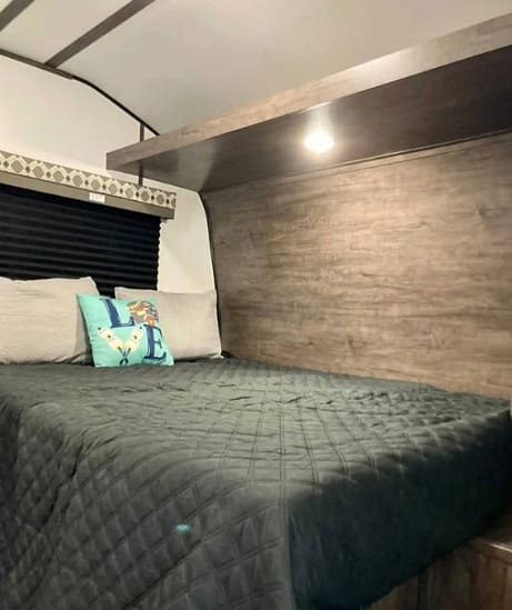 A bed in an RV with a bedside table.