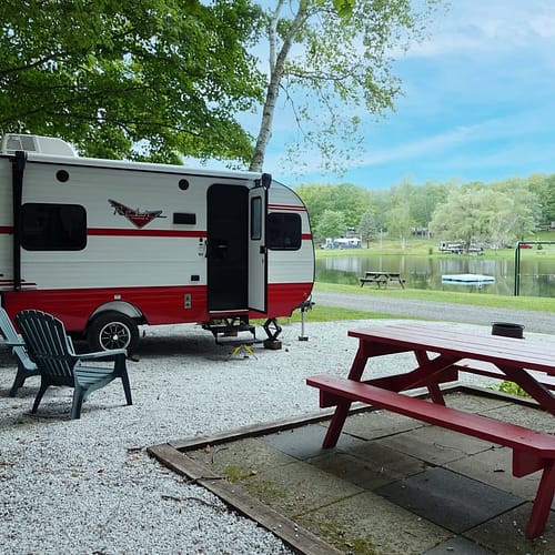 A camper parked in a gravel area next to a lake.