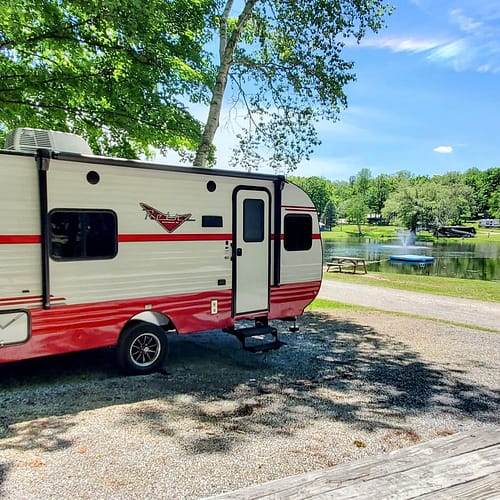 A red and white rv parked next to a lake.