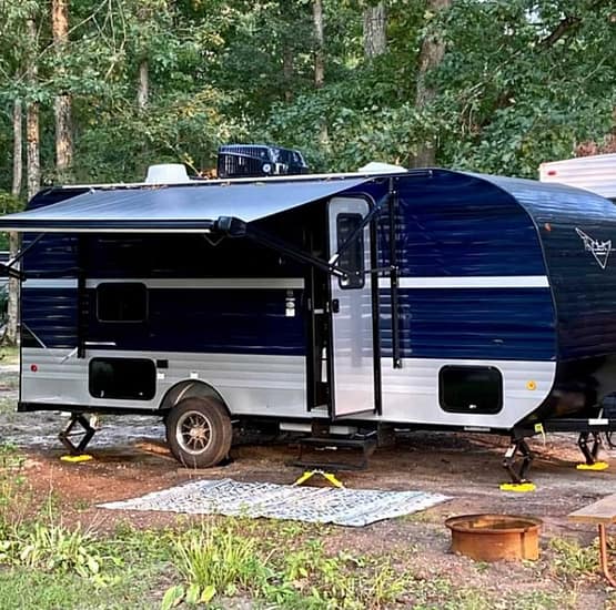 A blue and white RV parked in a wooded area.