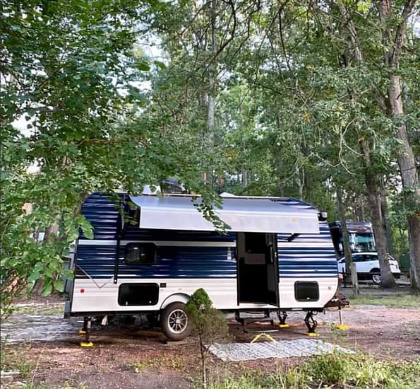 A blue and white RV parked in a wooded area, perfect for camping.
