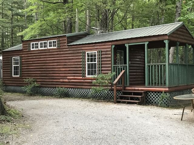 A log cabin with a porch and a gravel road.