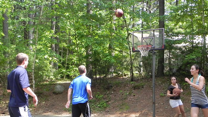 A group of people playing basketball in a wooded area.