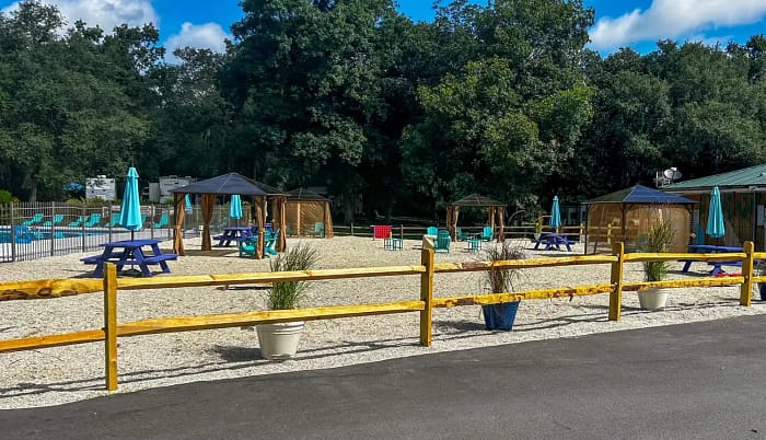 Outdoor seating area with picnic tables and gazebos, enclosed by a yellow wooden fence.