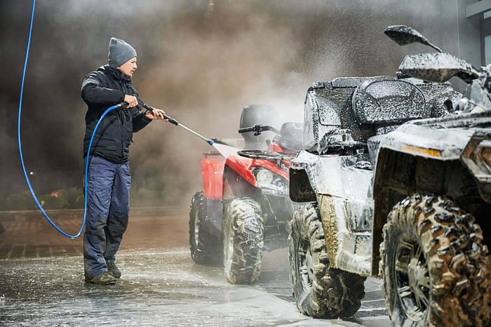 A man is washing his atv with a hose.