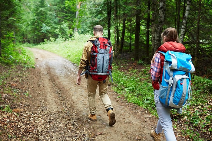 Two people hiking in the woods with backpacks.