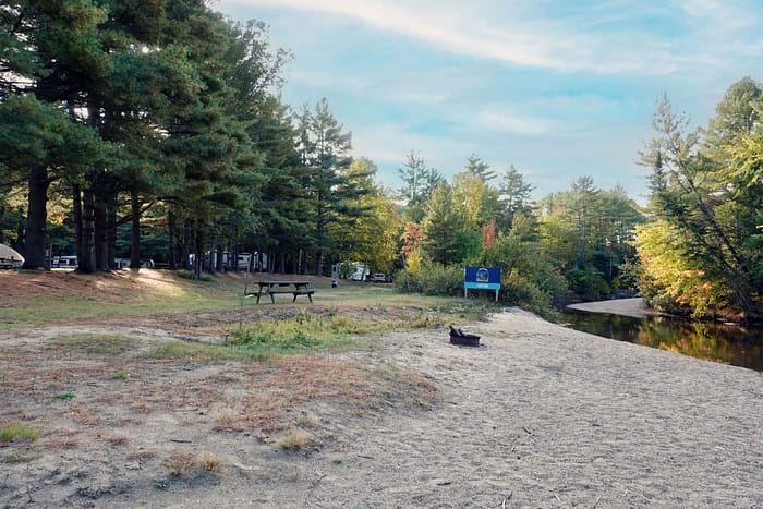 A sand beach with trees and a river in the background.