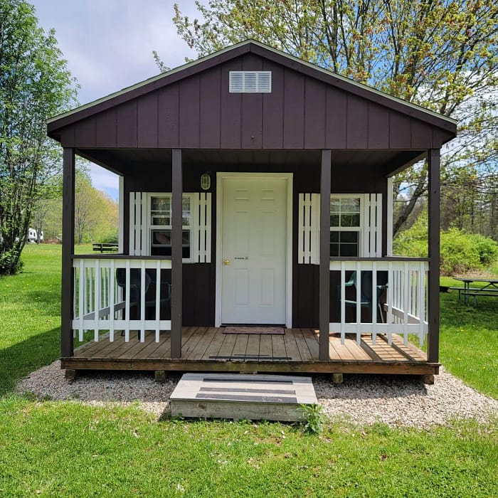 A small cabin with a porch nestled in a field.