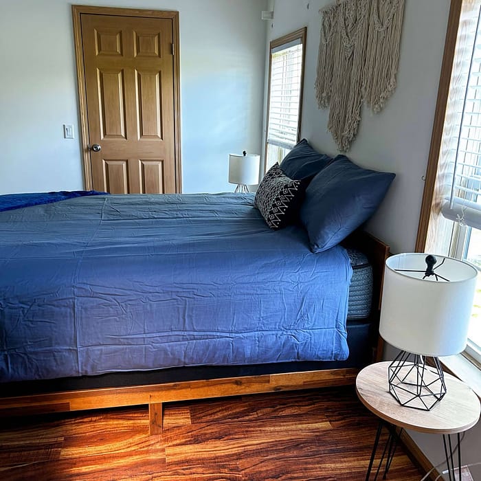A bed with blue sheets and a lamp.