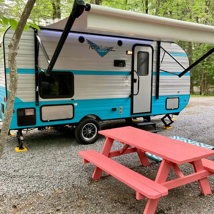 A camper parked in a gravel area with picnic tables.