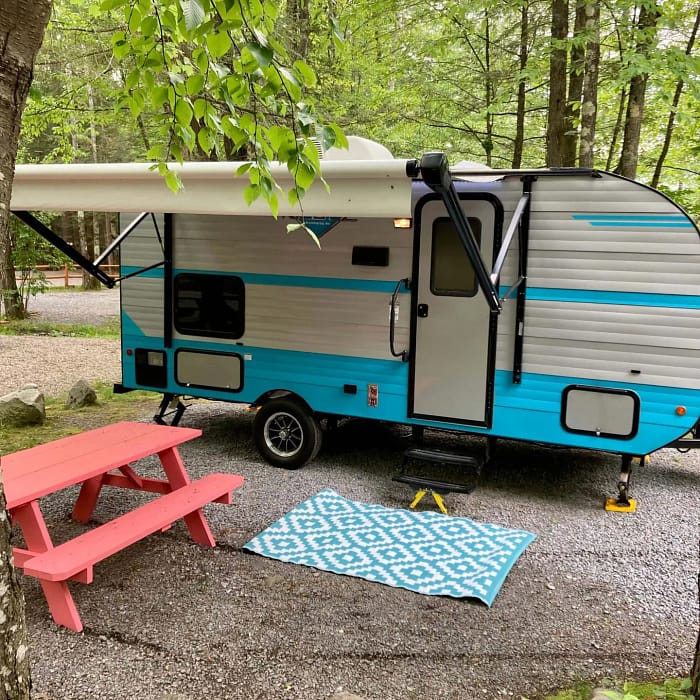 A blue and white camper parked in a wooded area.