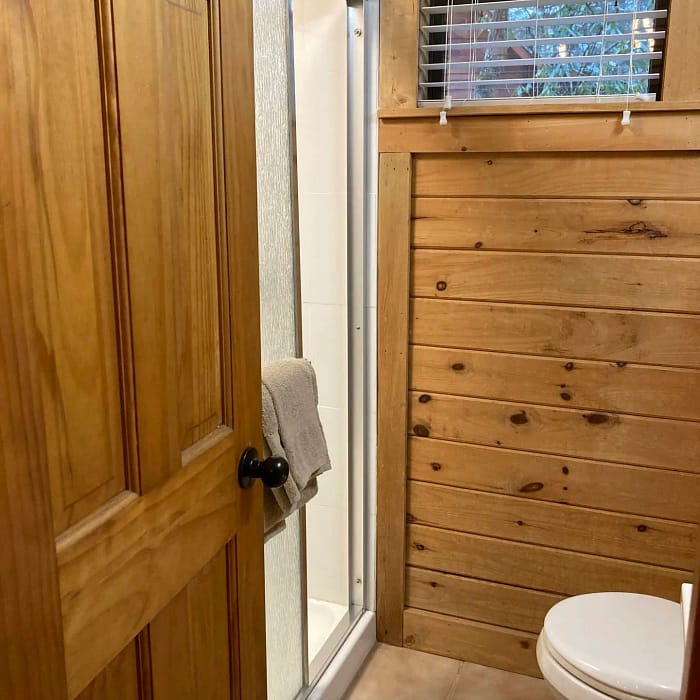 Interior of a bathroom featuring wooden cabinets, a shower stall, a toilet, and a window with closed blinds.
