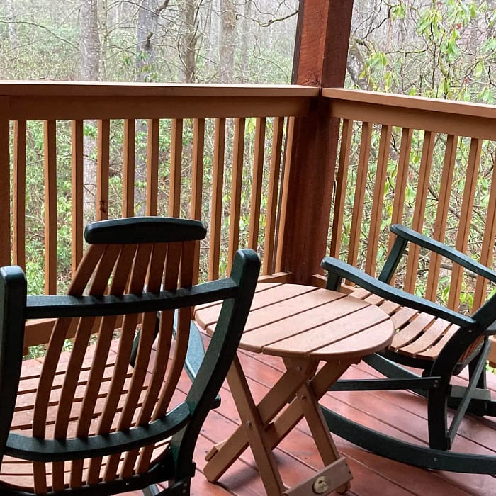 A wooden table and chairs on a forest-facing porch during a misty day.