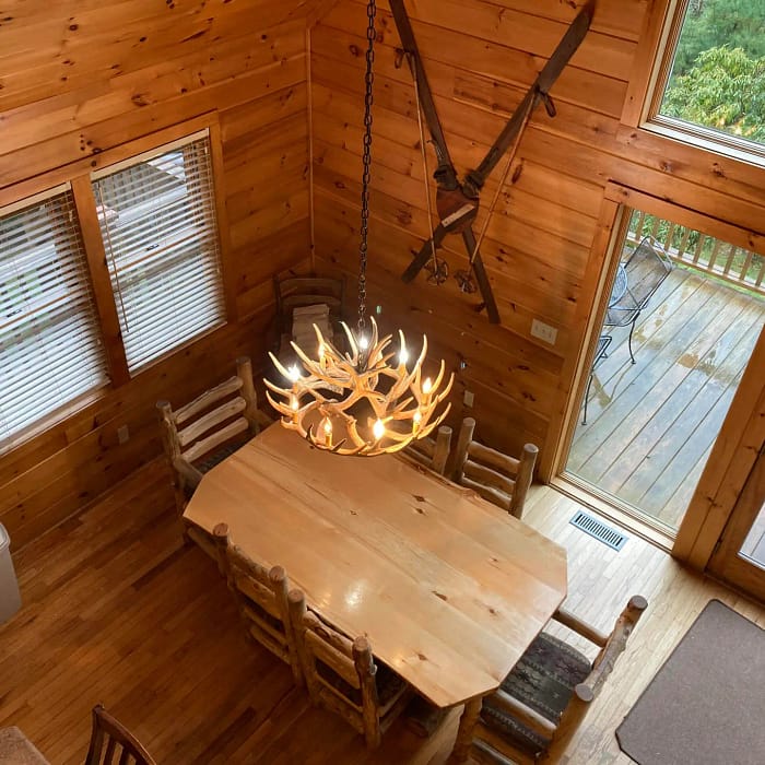 A rustic wooden dining area with a chandelier, featuring large windows and a high ceiling.