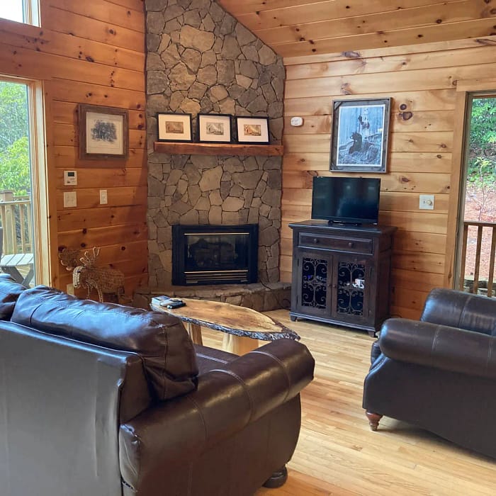 Cozy wooden cabin living room with a stone fireplace, comfortable seating, and a television.