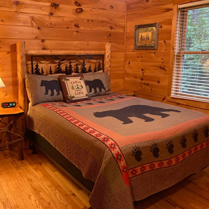 A cozy, rustic bedroom with a log cabin aesthetic, featuring a wooden bed adorned with bear-themed bedspread and pillows.