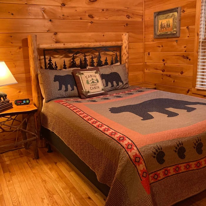 A cozy rustic bedroom with a bear-themed quilt and wooden cabin decor.