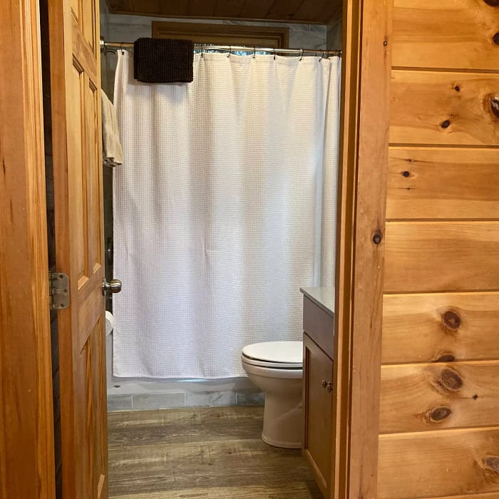A wooden-paneled bathroom with an open door, featuring a white toilet and a shower curtain.