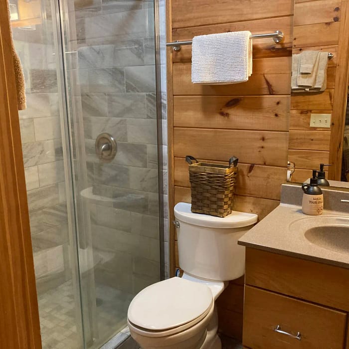 A bathroom interior with a glass shower enclosure, toilet, towel rack, and vanity sink with wooden cabinets.