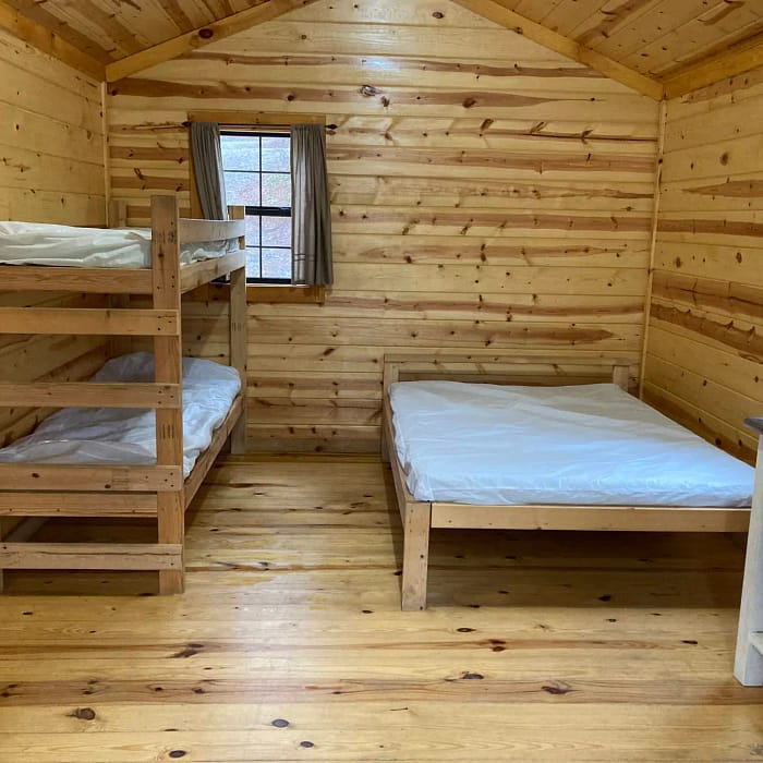 A wooden cabin interior with two bunk beds and a single bed, featuring a rustic design.