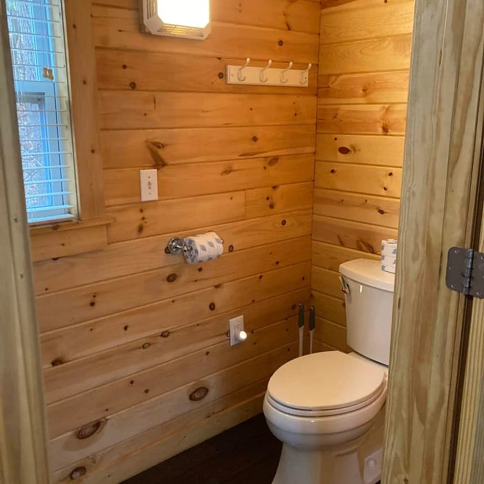 A small wooden-paneled bathroom with a toilet and a window.